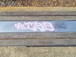 Offensive graffiti tags being removed from a public timber bench in Banksia Grove, Perth